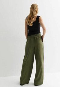 Olive green, wide-leg pants with an elastic waistband and a lightweight fabric. View from the back shows gathered waist and relaxed fit.
