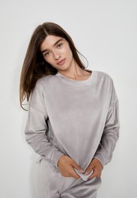 Maglietta a maniche lunghe in morbido velluto grigio chiaro con scollatura rotonda e vestibilità comoda, caratterizzata da spalle scese e polsini senza cuciture.