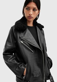 Μαύρη δερμάτινη μοτοσικλετιστική ζακέτα με μαλακό μαύρο γούνα από γιακά, υφή, ασύμμετρο φερμουάρ και πλαϊνές τσέπες.