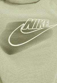 Hanorac verde deschis dintr-un material texturat, cu un logo alb Nike și un design cu dungi degradate în spate.