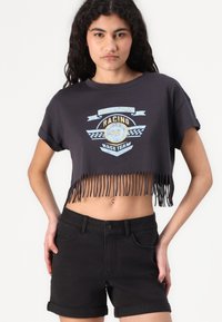 Maglietta nera corta con orlo frangiato e grafica da corsa. Presenta maniche corte e scollatura a girocollo. Abbinata a pantaloncini di denim neri.