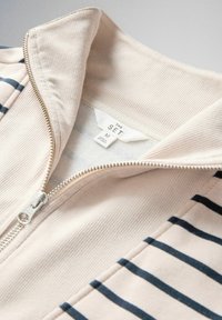 Bézs cipzáras dzseki tengerészkék vízszintes csíkokkal és bordázott gallérral, közepes méretű "THE SET" márkajelzéssel.