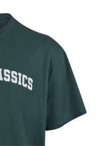 Sötétzöld pamut póló kerek nyakkivágással és rövid ujjakkal. A mellkason merész fehér "CLASSICS" felirat díszíti. Simára nyírt textúra.