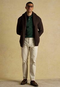 Tumepruun kootud salli cardigan rohelise polo särgi peal, koos kreemjatest pükstest ja pruunidest mokassiinidest. Tekstuuriga kangas koos taskutega.