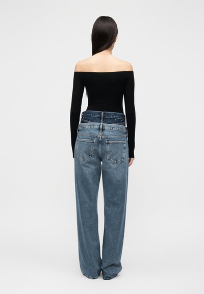 Μαύρο τοπ εκτός ώμων, σε συνδυασμό με άνετο, ανοιχτό μπλε τζιν με ψηλή μέση και μινιμαλιστικές λεπτομέρειες στην πίσω τσέπη.