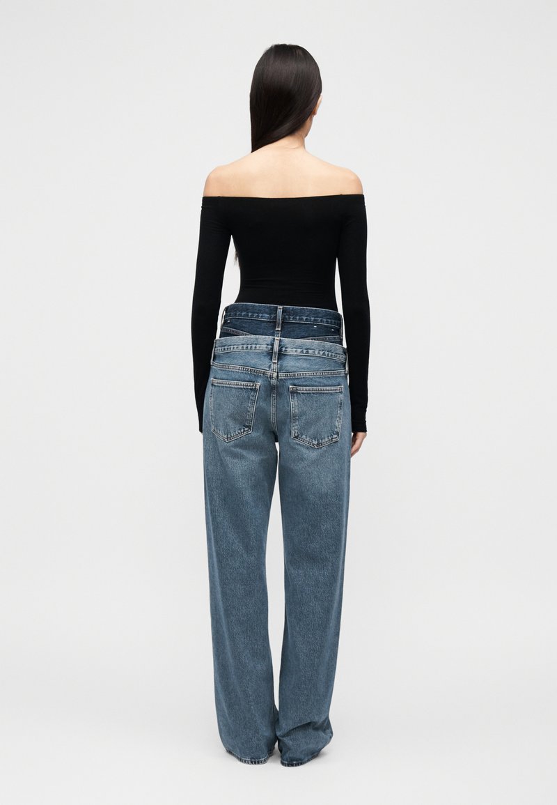 Haut noir à épaules dénudées, associé à un jean en denim bleu clair, ample, taille haute, avec un détail minimaliste sur la poche arrière.