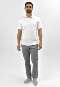 Witte polo met korte mouwen, voorzien van een drieknoopsluiting. Gecombineerd met lichtgrijze broek en grijze instappers.