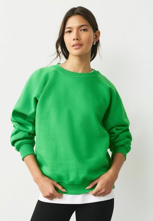 Grüner Sweatshirt mit rundem Ausschnitt, gerippten Ärmelbündchen und Saum. Bietet eine lässige Passform und weichen Stoff, getragen über einem weißen Lagenshirt.