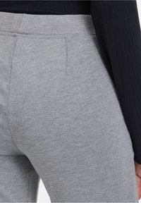 Šedé elastické kalhoty s hladkou texturou, mají široký pas a detaily na bočních švech. Materiál má jemný melírovaný vzor.