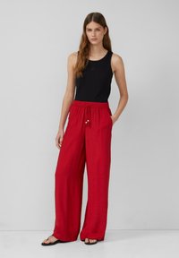 Débardeur noir et pantalon large rouge avec taille élastique et perles décoratives. Texture de tissu lisse, coupe décontractée et design casual.