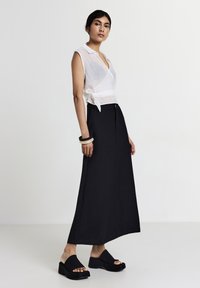 Weißes ärmelloses Wickeltop mit einem Bindungsdetail, kombiniert mit einem schwarzen Maxirock und schwarzen Plateausandalen. Glatte Texturen und klare Linien.