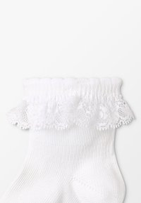 Calcetín blanco con textura acanalada, borde de encaje rizado en la parte superior y un cuerpo liso y sencillo que se extiende por el pie.