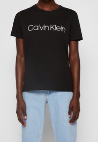 Černé bavlněné tričko s bílým logem "Calvin Klein". Krátké rukávy a kulatý výstřih; volný střih, hladká textura.