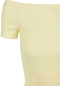 Haut jaune épaules dégagées en tissu côtelé, avec manches courtes et coupe ajustée. Texture lisse avec peu de coutures.