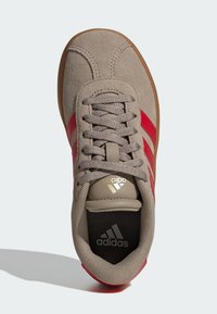 Bež antilop tenisica Adidas s crvenim prugama, bež vezicama i crnim unutarnjim đonom, prikazana iz ptičje perspektive na svijetloj pozadini.