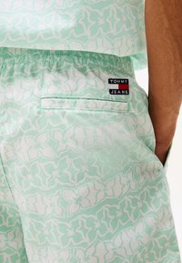 Pantaloni shorts verde menta con un motivo floreale bianco, vita elastica e una tasca posteriore con un'etichetta nera e rossa "TOMMY JEANS".