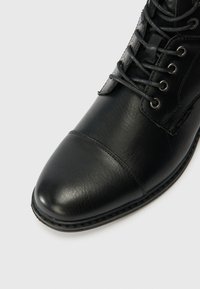 Botine negre din piele, cu vârful rotund, design cu șireturi, textură netedă și talpă plată. Include gromete metalice și detalii de cusătură.