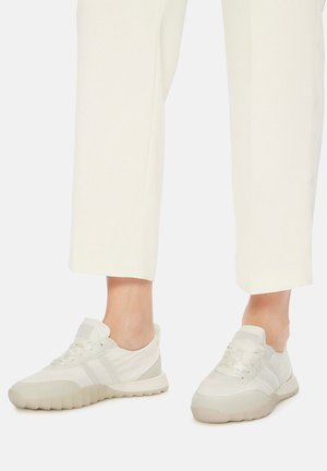 Bílé plátěné tenisky s texturovanou podrážkou, světle šedými detaily a šňůrkami. Nošené s širokými krémovými kalhotami, které zdůrazňují minimalistický design.