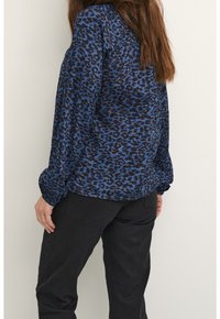 Blue leopard print blouse with long sleeves, elastic cuffs, and a relaxed fit, paired with black pants. Soft, textured fabric.