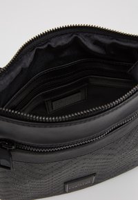 Černá kabelka z umělé kůže s prošívaným vzorem a zipovým uzávěrem. Uvnitř se nachází hlavní přihrádka a menší kapsa na zip.