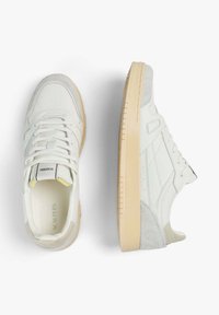 Zapatillas blancas con detalles de ante y malla. Diseño de punta redonda, suela plana de goma y acentos en marrón claro en la suela.