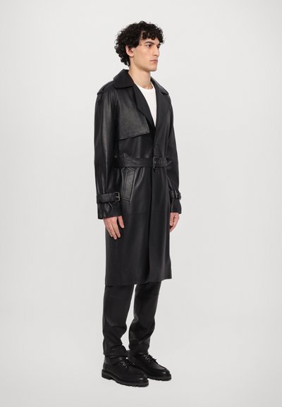 Svart läder trench coat med bälten i midjan, stor krage och långa ärmar. Har en dubbelknäppt front och sidofickor.