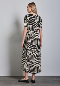 Zwarte en beige gestreepte jurk met korte mouwen, een gedefinieerde taille en een midi-lengte zoom. Platte zwarte schoenen maken de outfit compleet.