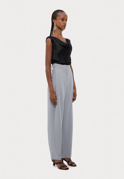 Top din satin negru cu guler cowl, asociat cu pantaloni gri cu talie înaltă și picior larg. Modelul poartă sandale negre cu bretele și cercei mari din aur.