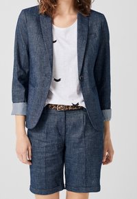 Jeansblazer med hakkkrage och uppvikta ärmslut, kombinerad med jeansshorts. Vit t-shirt med svart fågeltryck under, åtdragen med ett leopardmönstrat bälte.