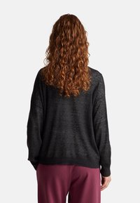 Černý, volný svetr s texturovaným pleteným vzorem, širokými rukávy a žebrovaným lemem, zkombinovaný s vínovými kalhotami.