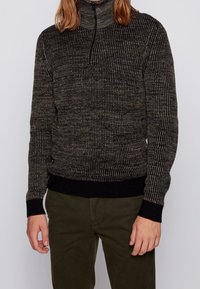 Stickad tröja med hög krage, med en strukturerad mörk design med ljusa prickar. Ribbad mudd och nederkant i enhetligt svart.