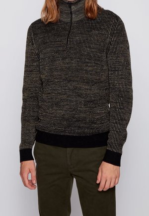 Pull en tricot avec un col montant, présentant un motif texturé sombre avec des nuances claires. Manchons et ourlet côtelés en noir uni.