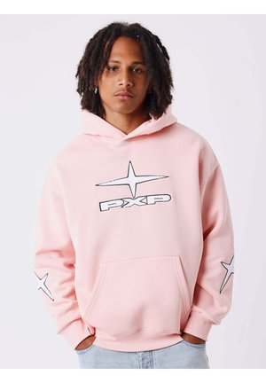 Jeune homme avec des dreadlocks aux épaules portant un sweat à capuche rose clair avec des motifs d'étoiles blanches et le texte "PXP" à l'avant.