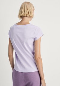 Kortærmet lilla T-shirt med rund hals, blødt bomuldsstof og sømdetaljer ved skuldrene, båret med lilla sweatpants.