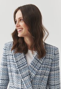 Blazer de tweed azul y blanco con un diseño estructurado, cuello con muescas y acabado texturizado, que presenta un patrón tejido y un ajuste a medida.