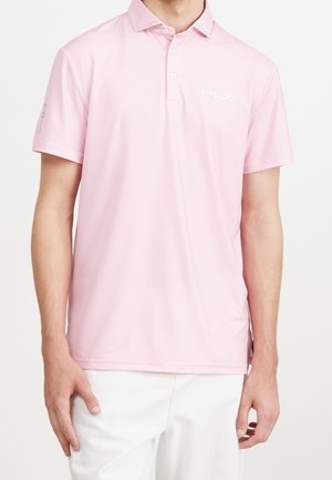 Mann trägt ein hellrosa kurzärmeliges Polo-Shirt mit RLX-Logo und weiße Hose, steht vor einem einfarbigen Hintergrund.