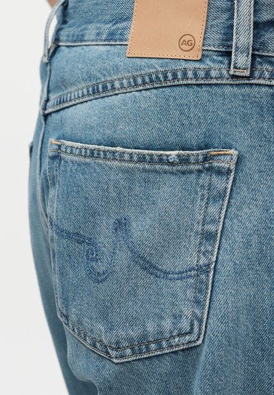 Κοντινό πλάνο σε τσέπη ανοιχτό μπλε τζιν με ραμμένο σχέδιο και ετικέτα από ταμπά δέρμα πάνω από τη μέση.