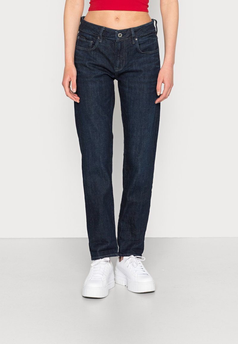 Mörkblå denimjeans med rak passform, fem fickor och knappstängning, tillsammans med vita platåsneakers.