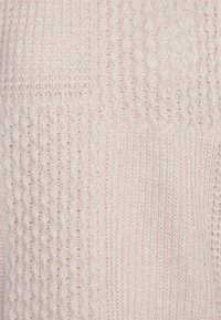 Tessuto a maglia di colore crema che mostra vari schemi di punti testurizzati, tra cui trecce e pizzo aperto.