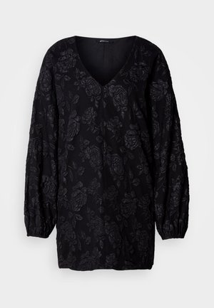 Čierna blúzka s dlhým rukávom a výstrihom do V, s textúrovaným kvetinovým vzorom. Rukávy sú na zápästiach nariasené pre voľný strih.