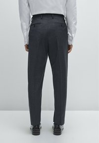 Dark gray tailored trousers with a smooth texture, featuring dual back pockets and pressed creases, paired with black leather shoes.