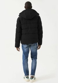 Chaqueta de plumas negra con capucha, con un diseño acolchado y puños elásticos. Combinada con jeans de mezclilla azul claro y zapatillas blancas con detalles en verde.