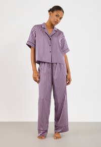 Fialový a biely pruhovaný pyžamový set s krátkym rukávom a gombíkmi na vrchu a širokými nohavicami s nastaviteľným pásom. Hladká textúra látky.