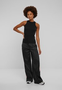 Top negru fără mâneci, cu un gât înalt, asortat cu pantaloni negri largi, cu dungi laterale. Țesătura pare netedă și ușoară.