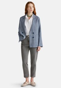 Světle modrý, texturovaný dvouřadý blazer s klopami, nošený přes bílou košili a šedé zúžené kalhoty. Bílé síťované nazouvací boty.