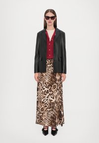 Blazer di pelle nera sopra un cardigan bordeaux, abbinato a una gonna maxi con stampa leopardata e ballerine nere con dettagli a fiocco. Occhiali da sole marroni.