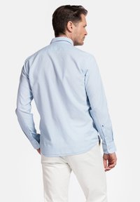 Lichtblauwe blouse met lange mouwen van zachte katoen, met een klassieke kraag, knoopmanchetten en een gebogen zoom, gedragen met crèmekleurige broek.