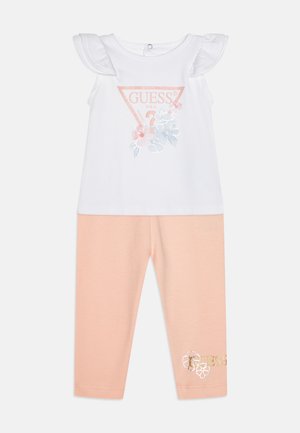 Bela majica z naborki in cvetličnim potiskom; roza legice z vezenim logotipom. Oba izdelana iz mehkega bombažnega blaga.