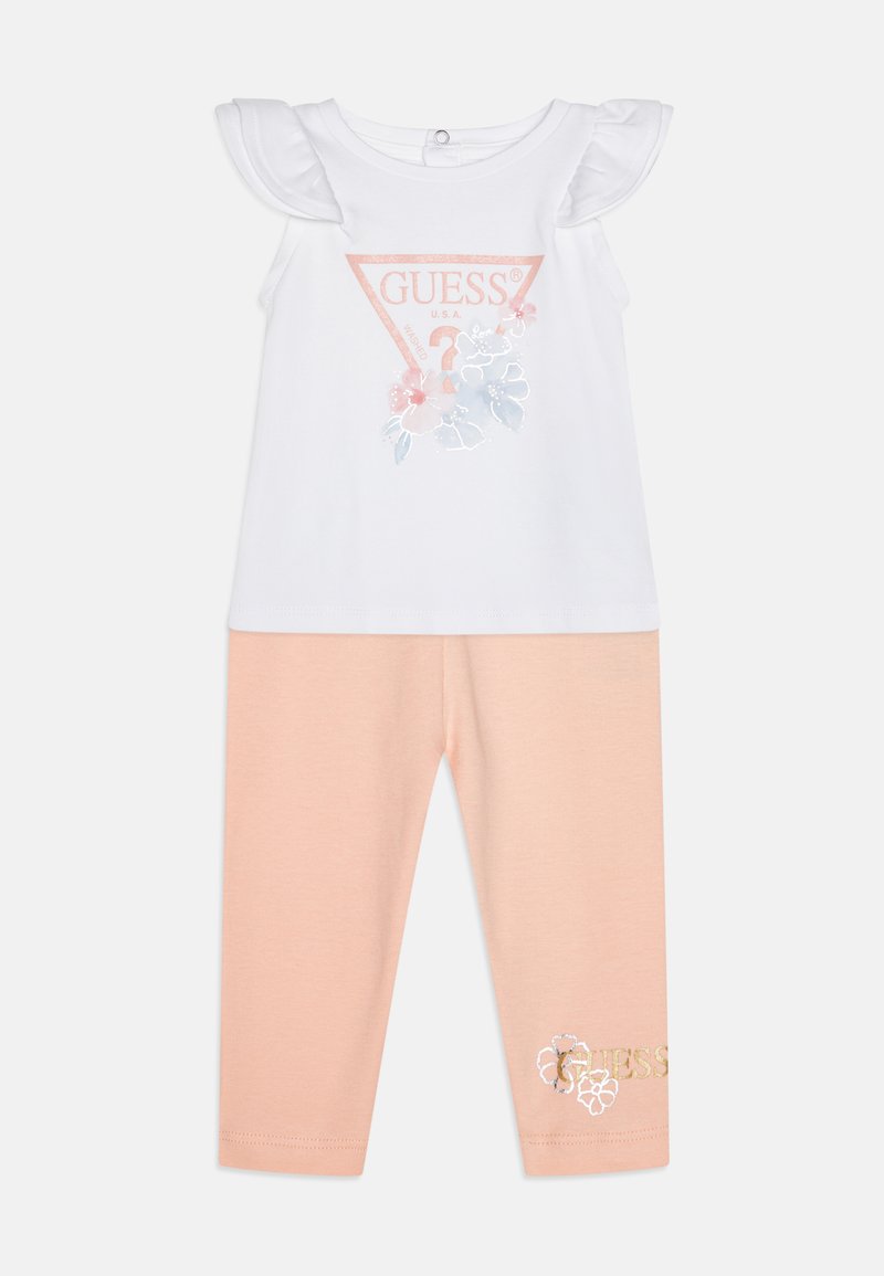 Witte top met rimpelige mouwen en bloemendessin; roze leggings met geborduurd logo. Beide gemaakt van zachte katoenstof.