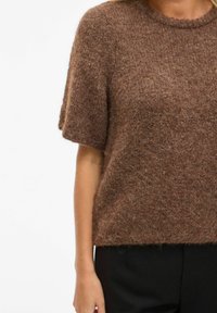 Brun strikket genser med korte ermer og rund hals. Myk tekstur med løs passform. Kombinert med svarte bukser.